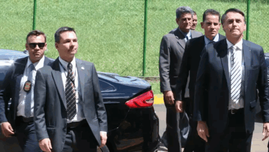 Vigiado por policiais, Bolsonaro aparece no jardim junto com o filho Jair Renan.